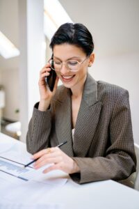 Confident businesswoman wearing glasses, talking on phone while reviewing documents in modern office setting.